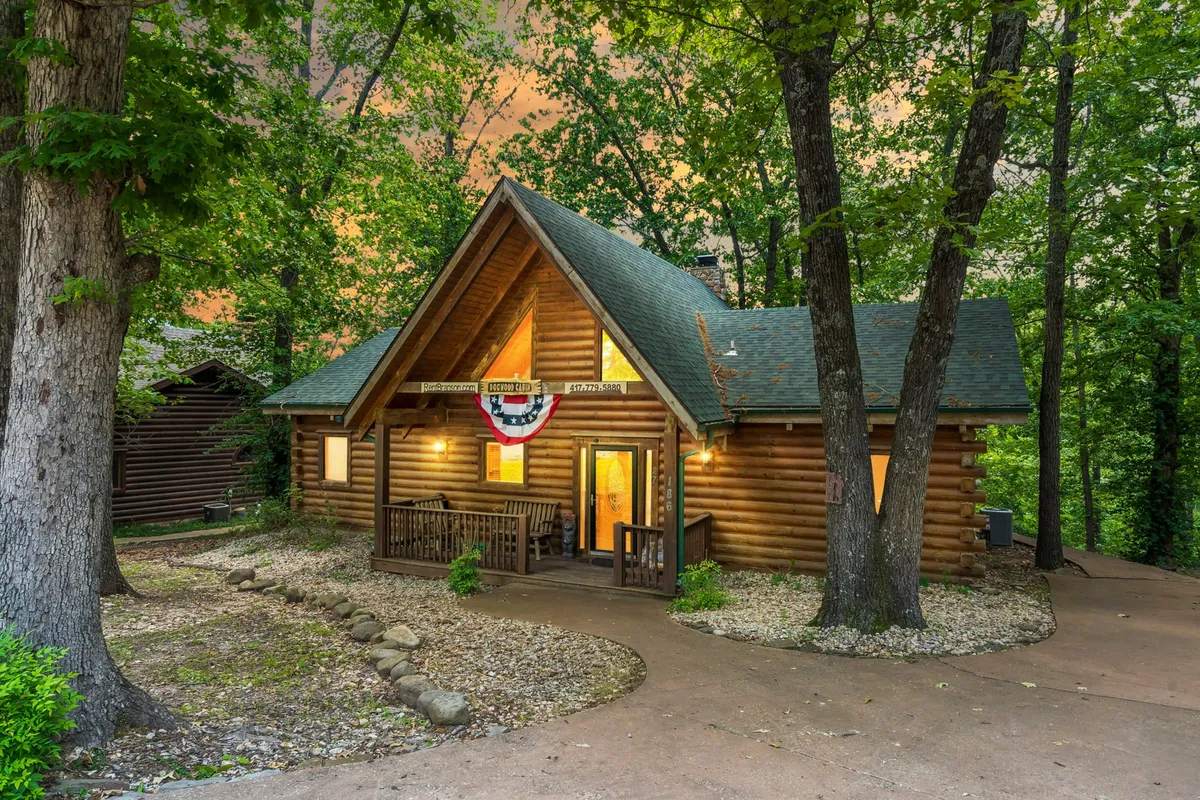 A charming log cabin exterior with a spacious front porch decorated with festive bunting. The setting suggests a cozy and inviting space perfect for family gatherings, outdoor barbecues, and creating memories in nature. The porch provides a prime spot for watching sunsets and relaxing after a day of adventure.