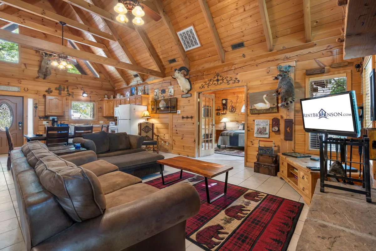 A homey living room scene with plush sofas, wooden beams, decorative mounts, a television, and a coffee table, all arranged for both relaxation and entertainment. The mood is cozy, inviting guests to relax, watch TV, or gather for games.