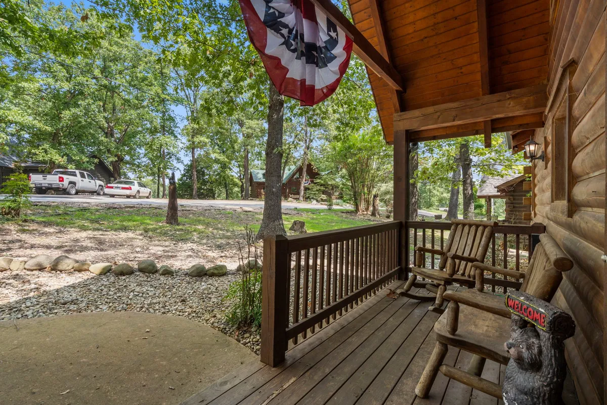 This exterior shot features wooden rocking chairs, a whimsical bear statue, flag banners, and lush greenery surrounding the cabin’s porch. The scene conveys a relaxed, welcoming vibe, ideal for unwinding as a group after an event or concert at Thunder Ridge.