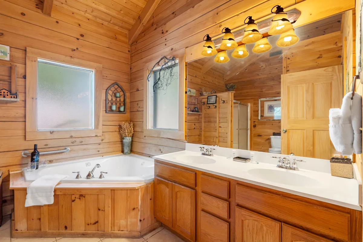A serene bathroom with a large bathtub, double sinks set in a wooden vanity, warm lighting, and a wide mirror. The space exudes tranquility and is perfect for morning routines or unwinding together.