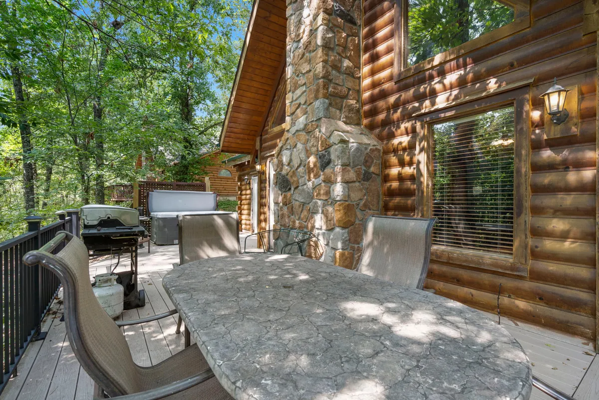 An outdoor dining space featuring a grill, a sturdy dining table, and a stone chimney, all nestled among tall trees. The setting suggests opportunities for both morning coffee and lively barbecues in a natural environment.