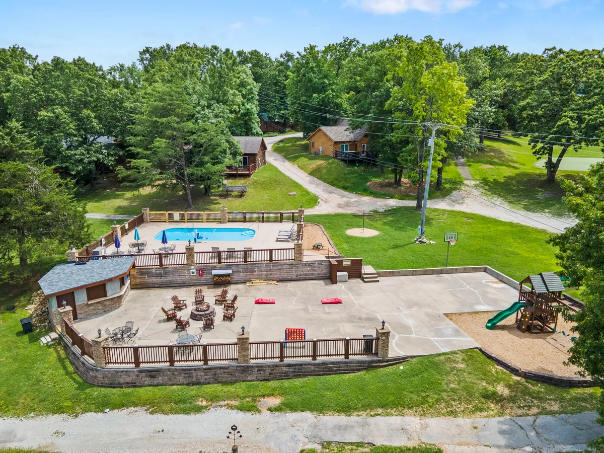 This exterior image showcases a swimming pool surrounded by lounge chairs, a playground area, and a basketball hoop, with green trees framing the family-friendly setting. Children can be seen playing, and the pool area radiates a relaxed, inviting atmosphere.